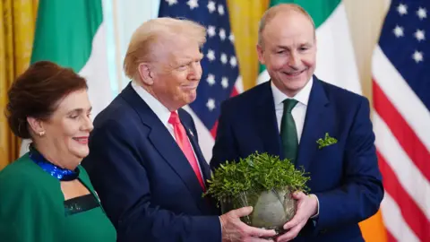 The Taoiseach of Ireland Micheal Martin (R) and his wife Mary O'Shea (L) present US President Donald Trump with the traditional shamrock bowl during a St Patrick's Day reception at the White House in Washington DC