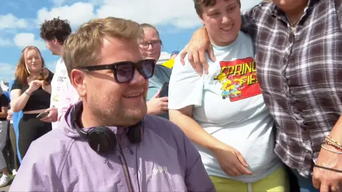 James Corden wears a headset and sunglasses as he greets fans in Barry Island