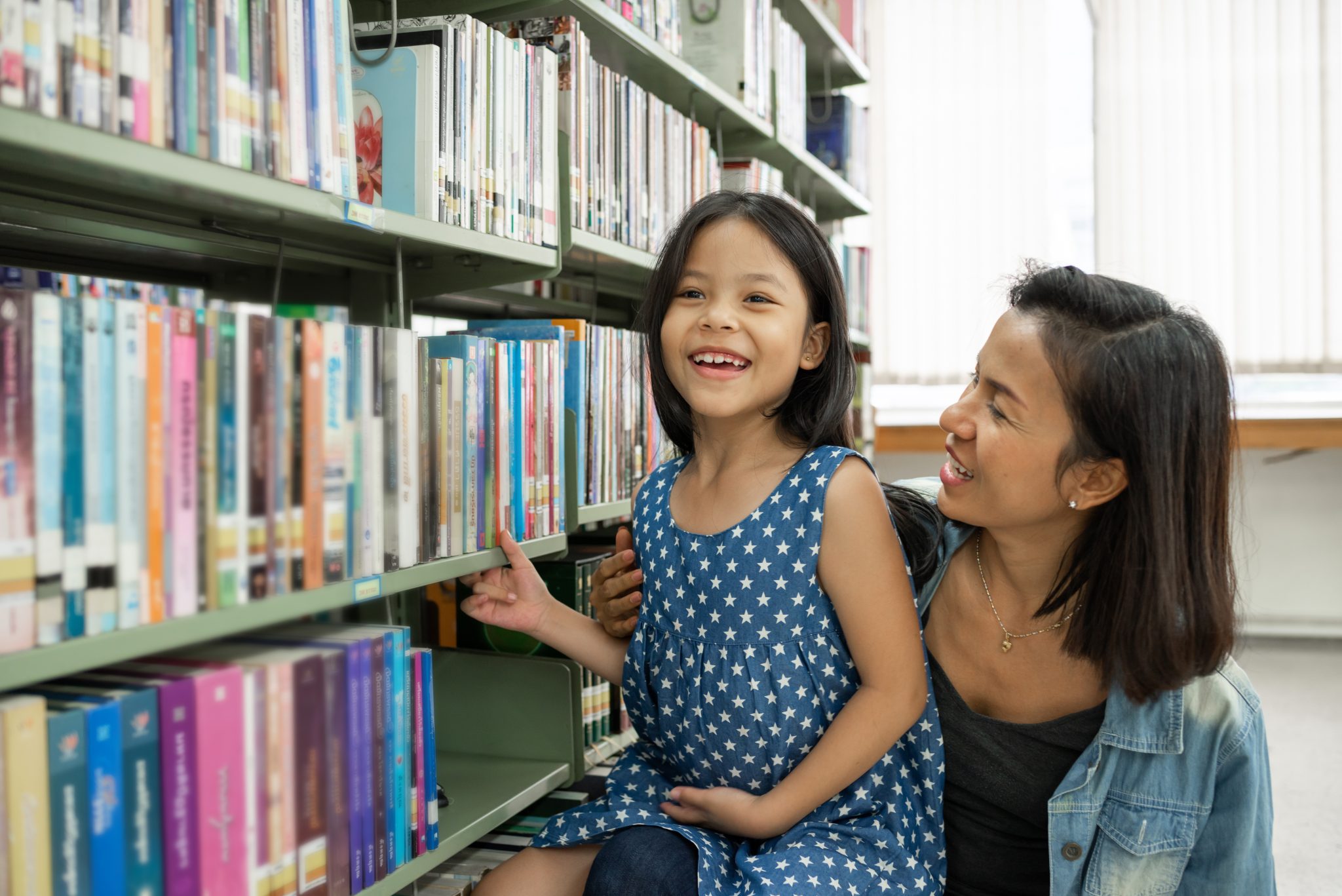 A mother and her child smiling next to a library bookshelf.