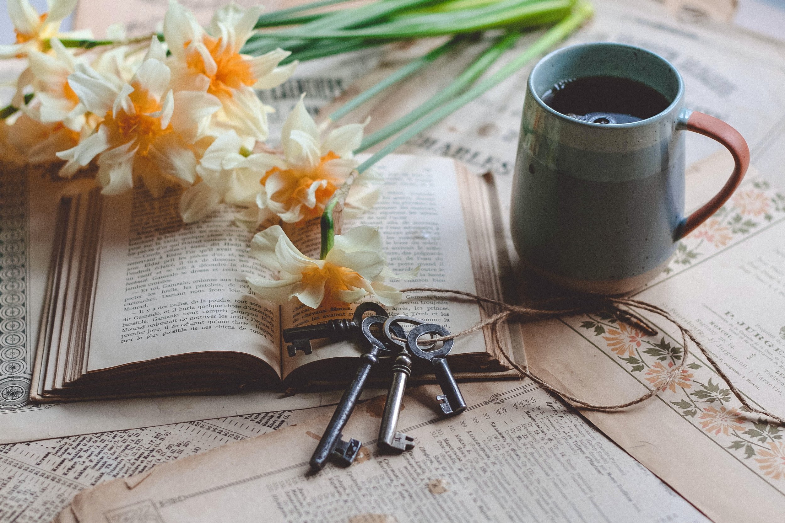 A photo of an old book, flowers, and a cup of coffee