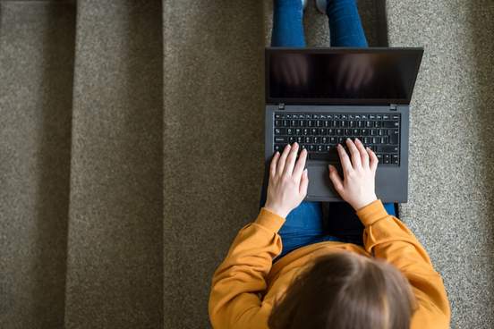 overhead photo of a person seated on stairs using a laptop 