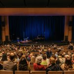 View of the Desautels Concert Hall stage from the upper back of the hall with audience members in their seats.