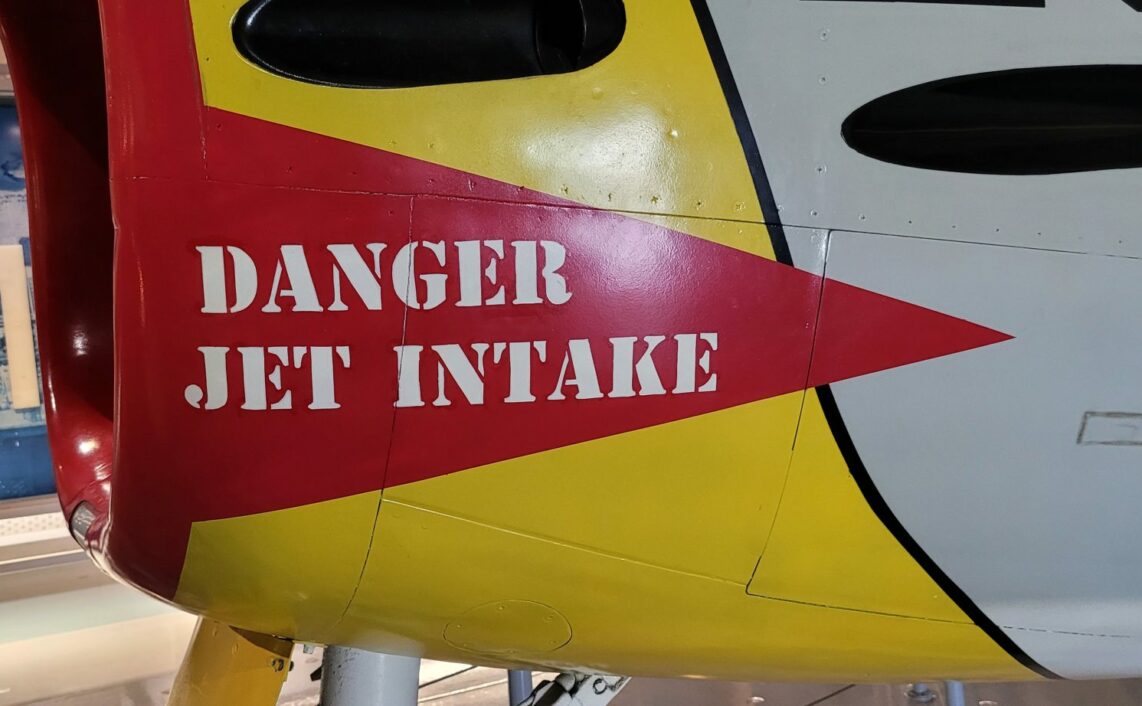 Photo of the air intake of a jet fighter, with a sign saying "danger, jet intake".