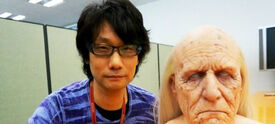 Hideo Kojima standing next to a bust of Code Talker.