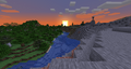 River running between a forest and a windswept hills biome with a sunset in the background.