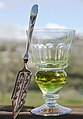 An absinthe glass with naturally-colored absinthe (verte) with an absinthe spoon.