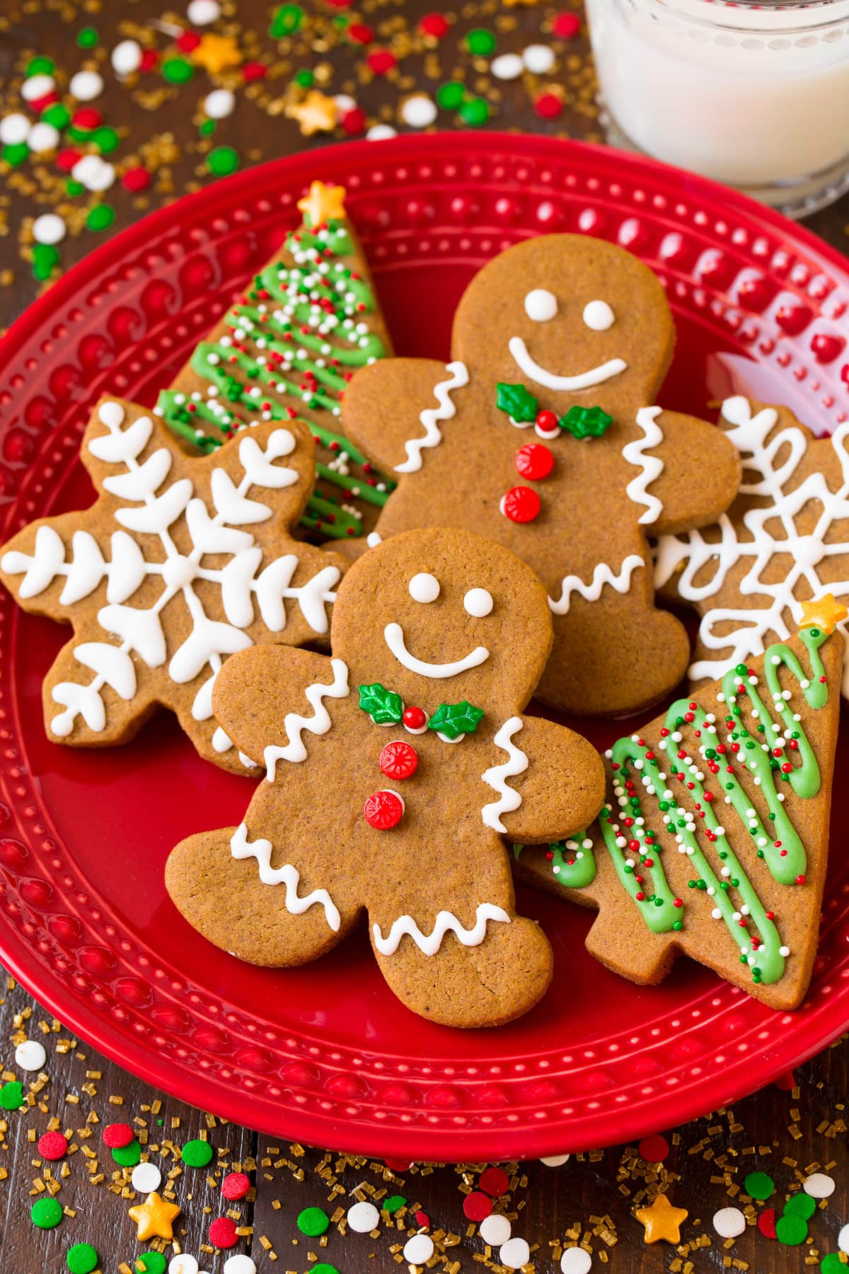 Gingerbread men cookies and trees and snowflakes on a red plate surrounded by Christmas sprinkles.