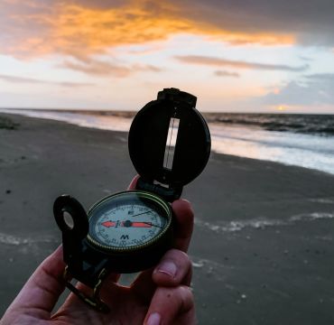 En hånd holder et kompass på en strand med havet i bakgrunnen