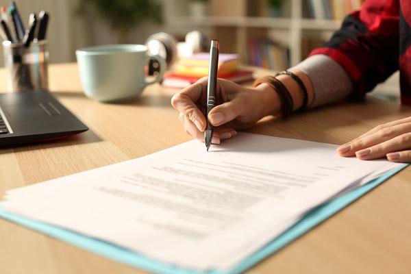 Close-up of hand writing on documents with pen.