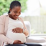 Pregnant woman on sofa smiling down at her belly.