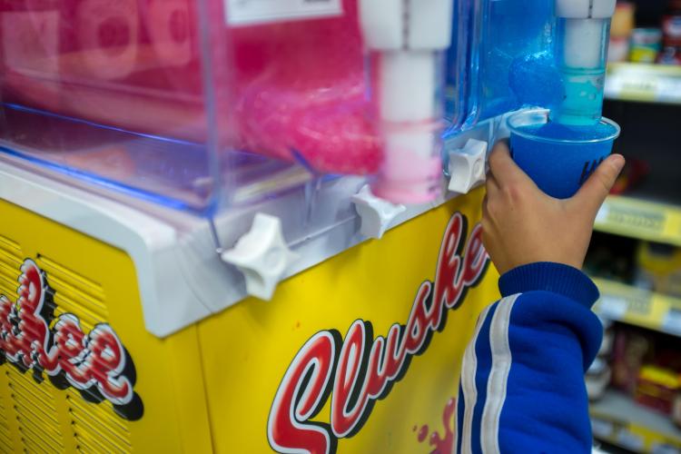 Child using a slushy machine in a convenience store.